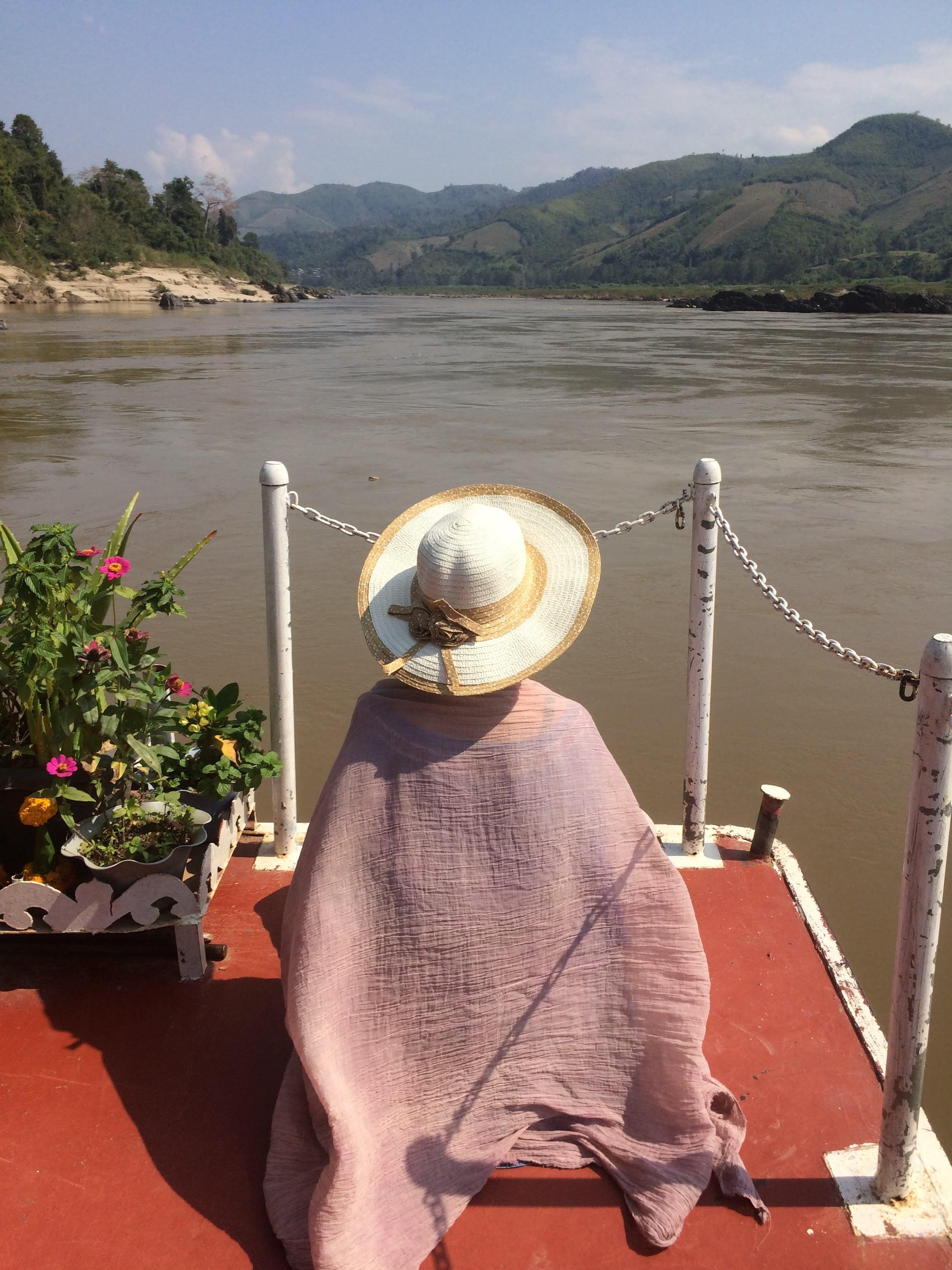 View from the bow of a slow boat on the Mekong river in Laos, looking toward green mountains